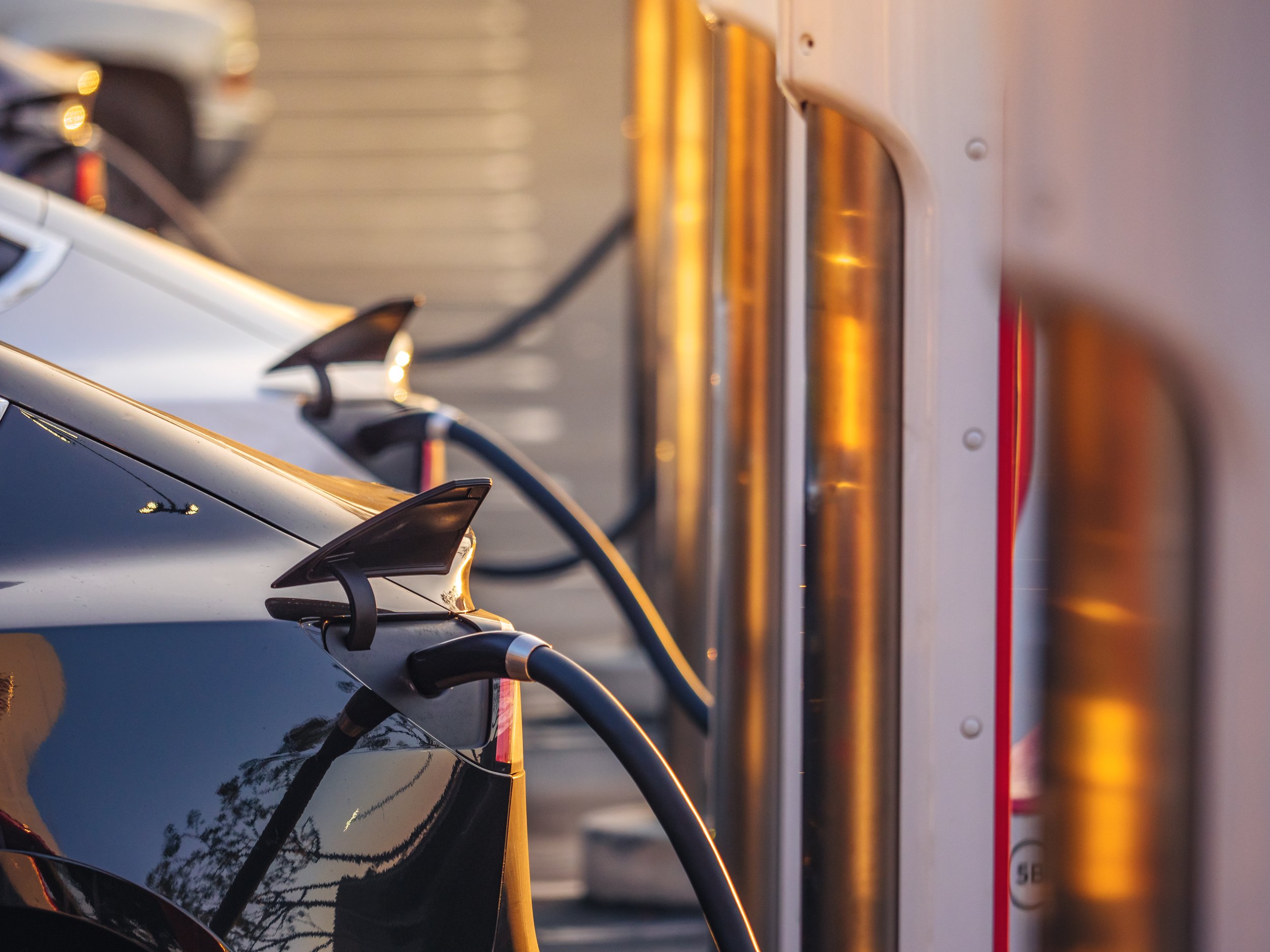 Electric cars charging at charging station outdoors at sunset - 24x7 Electrical Services