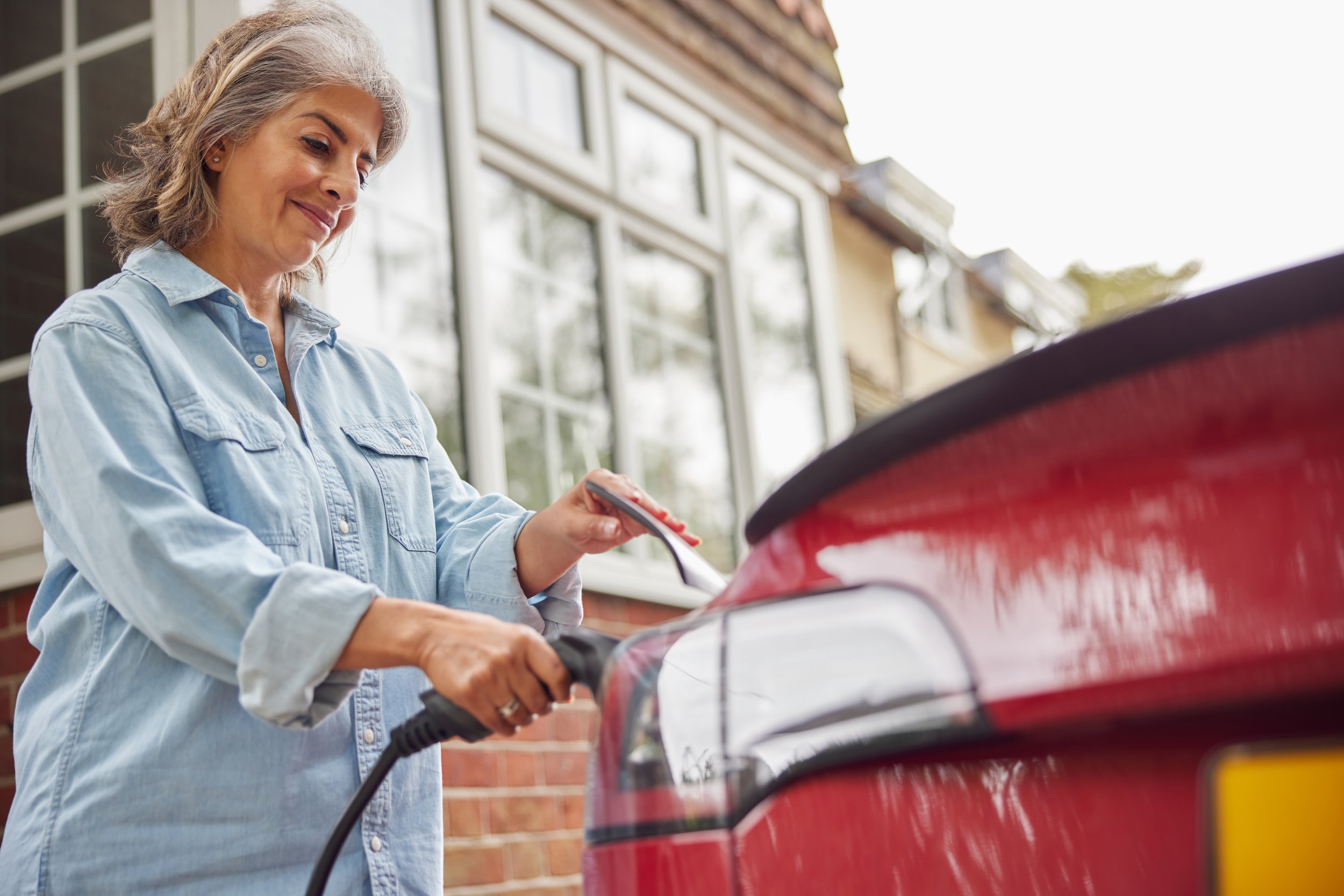 Mature Woman Attaching Charging Cable To Environmentally Electric Car At Home from 24x7 Electrical Services